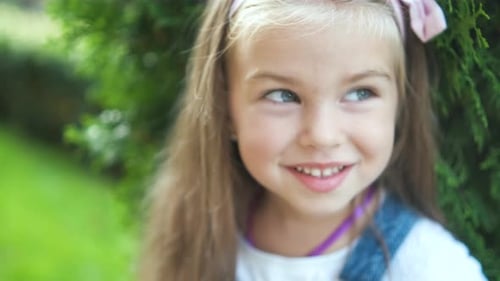 Portrait of pretty child girl standing outdoors in summer park smiling happily.