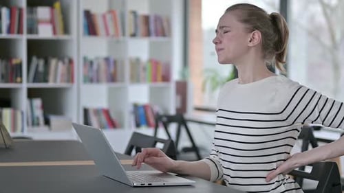 Young Woman with Back Pain Using Laptop in Library