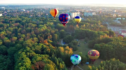 Beautiful sunbeams illuminate the balloons that fly over the park, green trees.