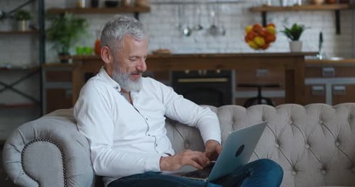 Smiling Man Relaxing on Sofa Using Laptop
