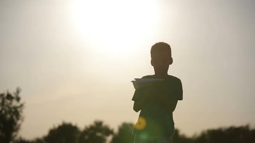 Boy Silhouette Launches Paper Airplane at Sunset