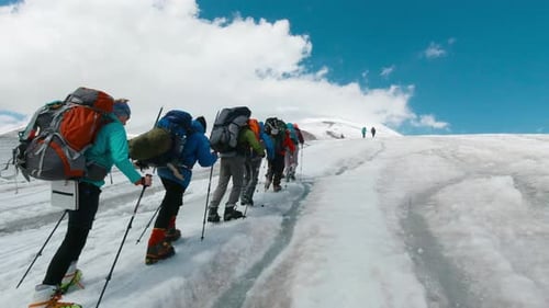 Climbers follow each other in line to snowy peak on a clear day