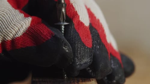 Close Up of Gloves Screwing Screw Into Wood