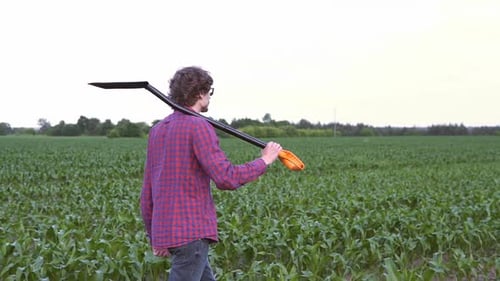 The farmer holds a shovel in his hand on an agricultural field, harvest time.