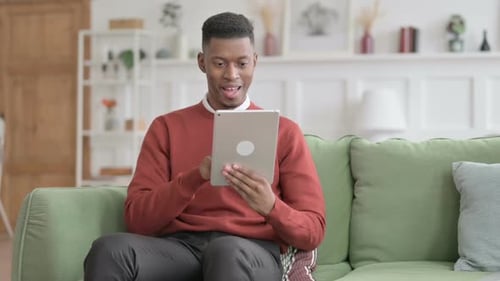 Man Celebrates Good News on Tablet at Home