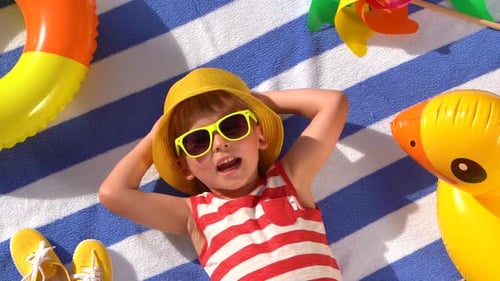 Boy Lying on Towel with Beach Toys