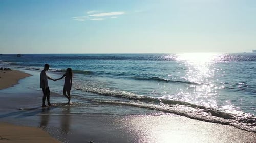 lovely young couple relaxing on the sandy beach on a sunny day. Direct sunlight. Woman pulling her b