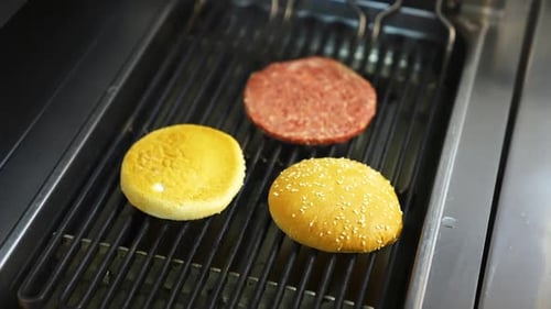 Two burger buns and one cutlet are being cooked on a barbecue grill