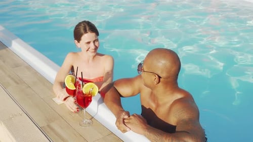 Happy Multiethnic Couple Clinking Glasses in the Swimming Pool