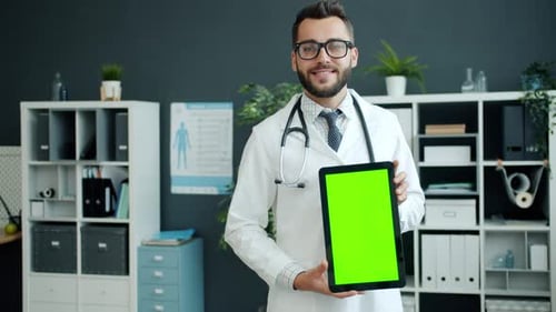 Cheerful Young Man Doctor in White Gown Is Holding Tablet with Green Chroma Key Screen Smiling