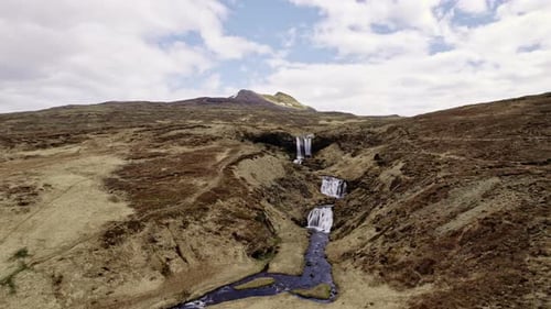 Scenic Aerial Shot of Majestic Waterfalls in the Middle of a Rocky Green Fields