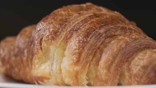 Croissant auf weißem Teller rotierend vor der Kamera auf schwarzem Hintergrund
