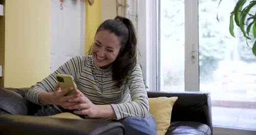 Woman Laughs While Using Smartphone on Sofa