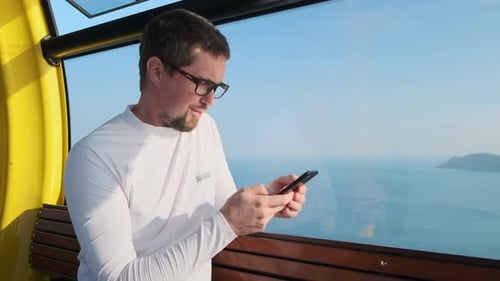 Man Using Phone in Scenic Cable Car
