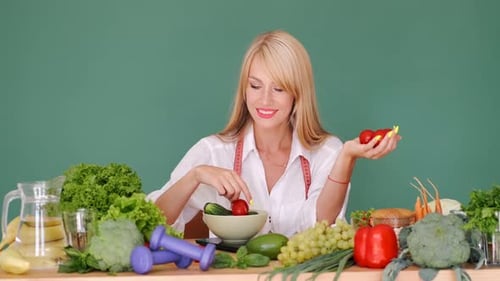 Fit Woman Measuring Vegetabes on Scales at a Table on Green Background