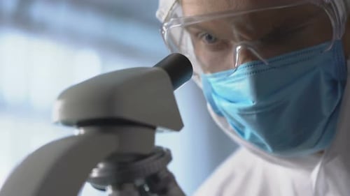 Scientist Looking Through Microscope in Protective Suit