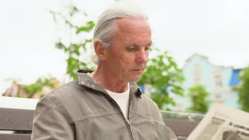 Handsome Grayhaired Man Sitting on the Bench Early in the Morning and Reading Newspaper in Park