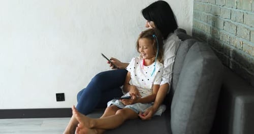 Mother and Daughter Relaxing with Smartphones on Sofa