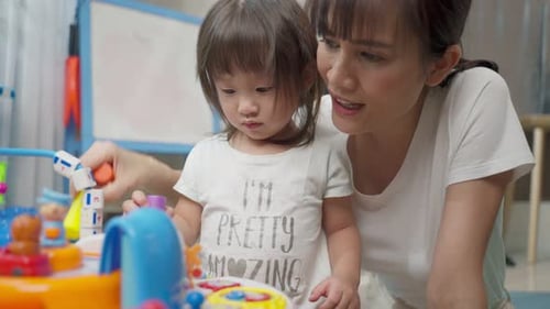 Asiatische glückliche Familie, schöne Mutter und kleines Mädchen spielen zusammen Spielzeug im heimischen Wohnzimmer