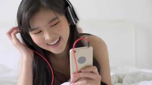 Girl Listening to Music with Headphones in Bed