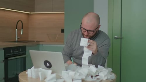Young Adult Man Accounting Home Budget with Lots of Store Receipts on the Table