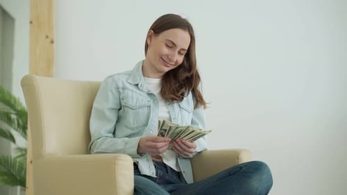 Woman Counts Money Sitting in a Chair in the Living Room at Home