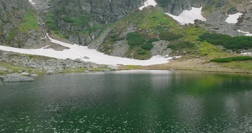 flying over a blue crystal clear mountain lake in mountains with some snow