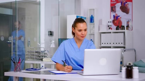 Woman in Scrubs Working on Laptop in Doctor's Office