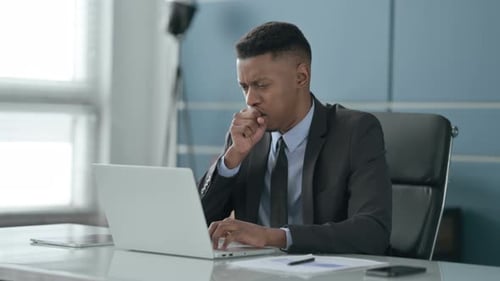 African Businessman Coughing while using Laptop in Office