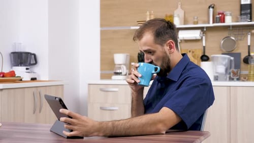 Man Using Tablet While Drinking Coffee in Kitchen