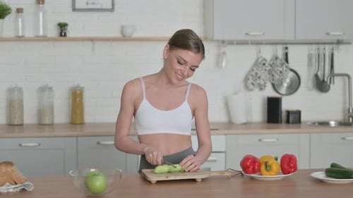 Woman Smiling Cutting Cucumber in Kitchen