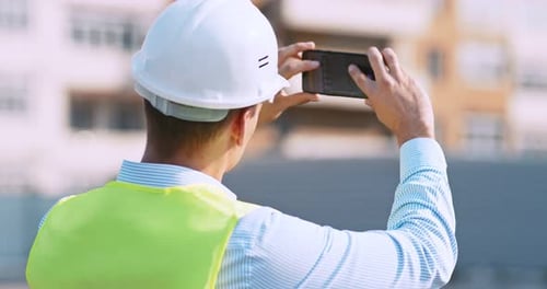 Worker at Construction Site Making Photos on His Cell Phone, Back View, Tracking Shot