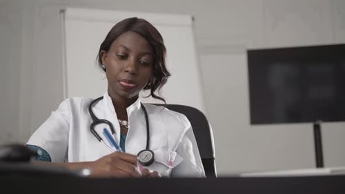 Female Doctor Writing at Desk in Office