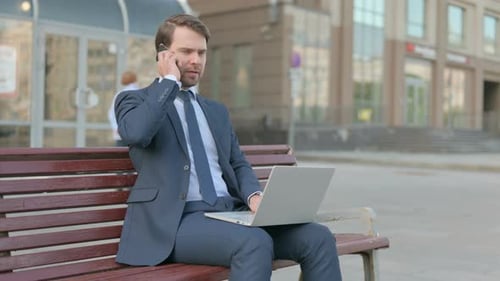 Man Working on Laptop and Phone on Bench