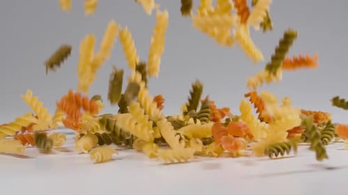 Colorful Tricolor Rotini Pasta Falling onto White Surface