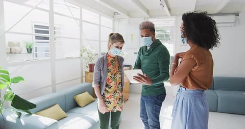 Office colleagues wearing face mask discussing over digital tablet at office
