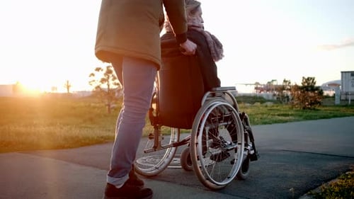 Careful Man Is Rolling Invalid Carriage with Woman in Garden Lifting Wheels