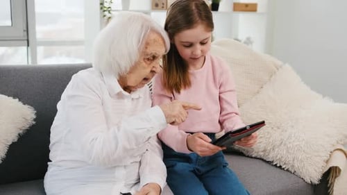 Girl Showing Senior Woman Tablet Indoors on Couch
