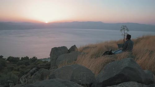 Man Uses Laptop on Hill at Sunrise