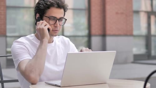Young Man Talking on Phone with Laptop Outdoors
