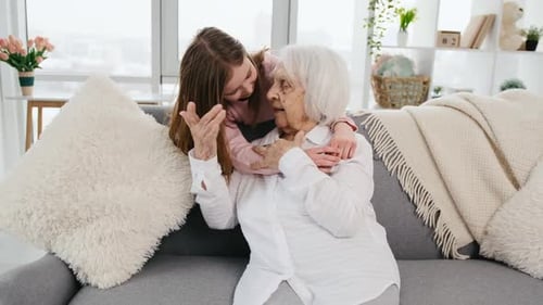 Child Hugs Senior Woman on Couch Indoors