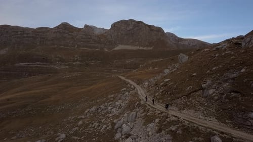 Three Cyclist Ride Bike on Path in Rocky Steep Hills Mountains in Autumn