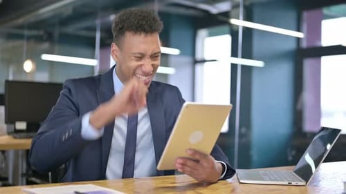 Young Businessman Celebrating Success on Tablet in Office