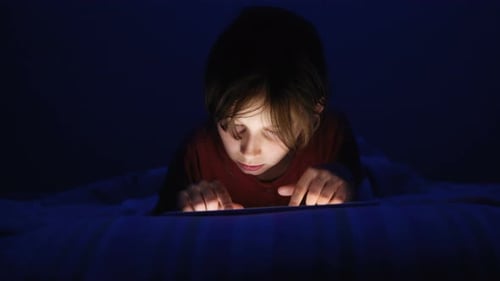 Kleines Mädchen liegt im Bett und spielt Tablet im sozialen Internet in dunkelblauem Licht