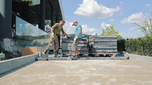 Road Workers are Laying Paving Stones and Building a House