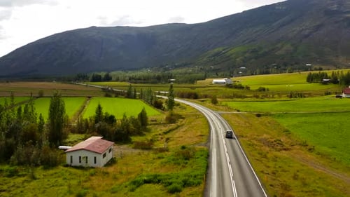 Scenic Aerial Drone Shot Of Car Driving Down Lonely Country Road Surrounded By Nordic Farm Fields