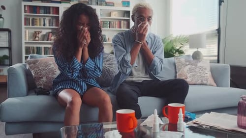 Couple Sick on Couch at Home Wiping Noses