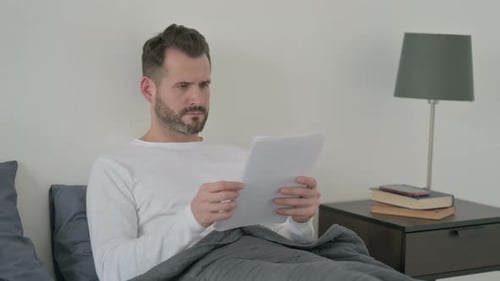 Man Reading a Document in Bed Indoors