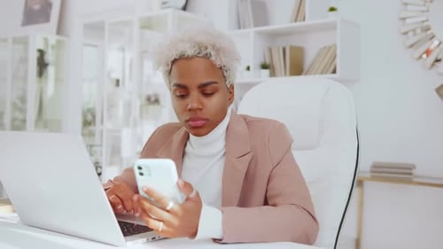 African American Woman Entrepreneur Works with Phone and Laptop Sits in Office