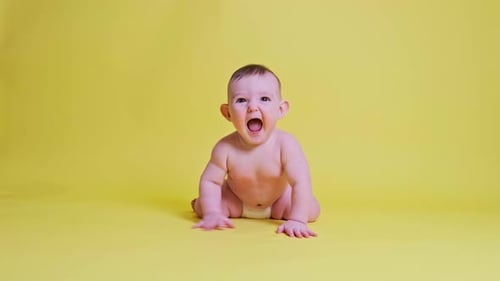 Happy toddler baby plays laughing on studio yellow background